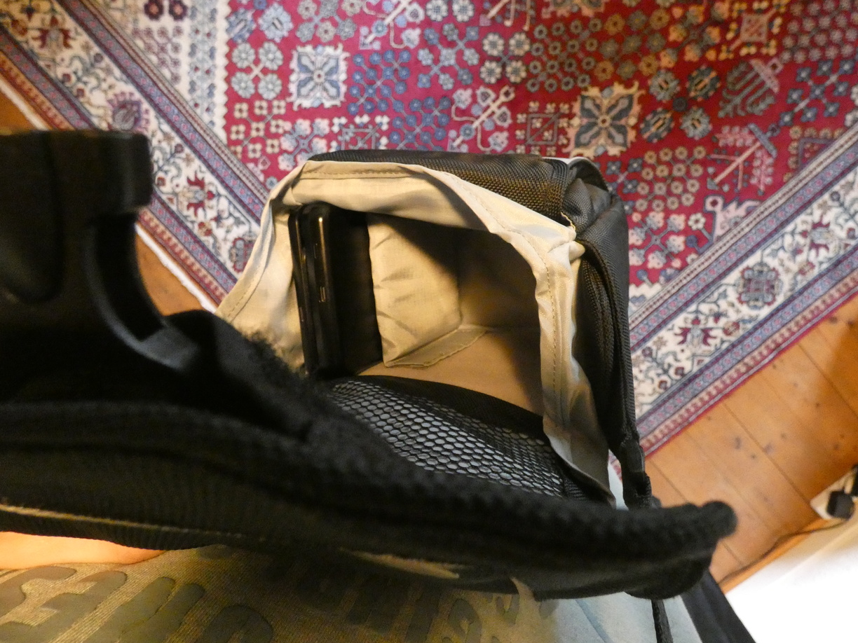 A photo taken in first person view, displaying a photo bag hanging from my shoulders. It’s held open by my left hand. The main compartment is split into two with a separator. The small compartment was adjusted to be as big as the PPKB, making it fit perfectly.