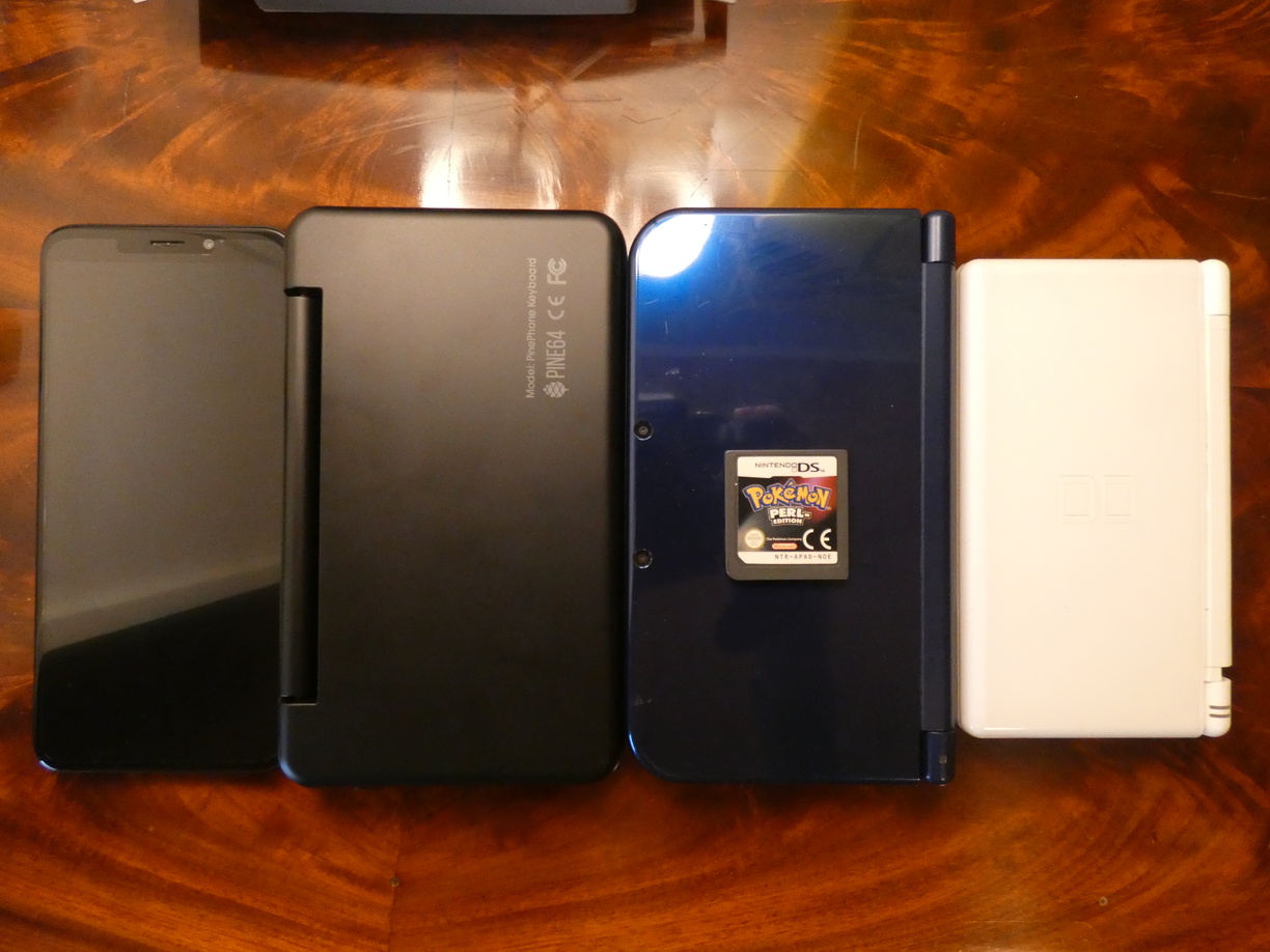 A photo of four devices next to each other on a table in portrait rotation: The PinePhone, the keyboard case which is a bit wider and a lot thicker, a New Nintendo 3DS XL which is nearly exactly as big as the keyboard case, only a bit thicker, and a smaller Nintendo DS Lite.