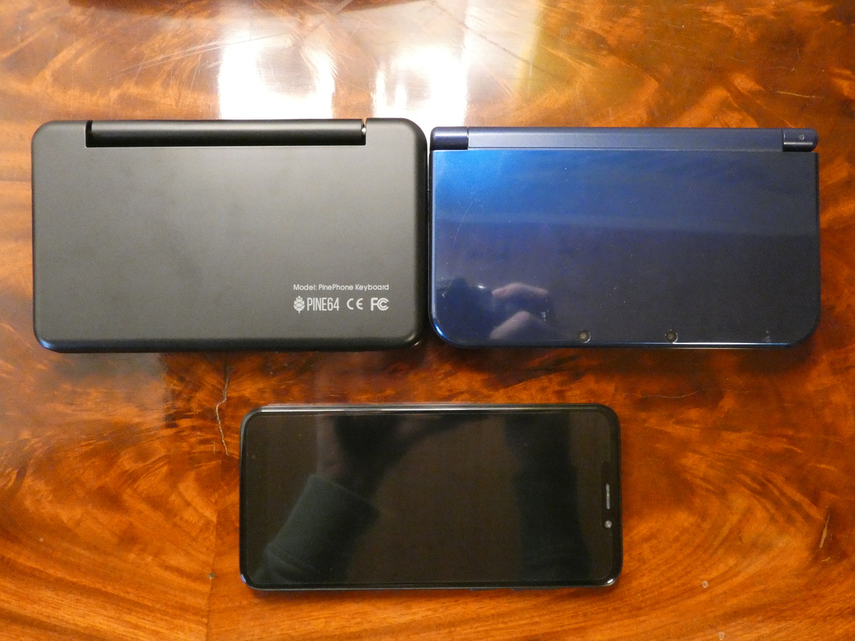 A photo of three devices (now without the DS Lite) next to each other on a table, this time in landscape rotation so the very similar length of the shorter side can be compared.