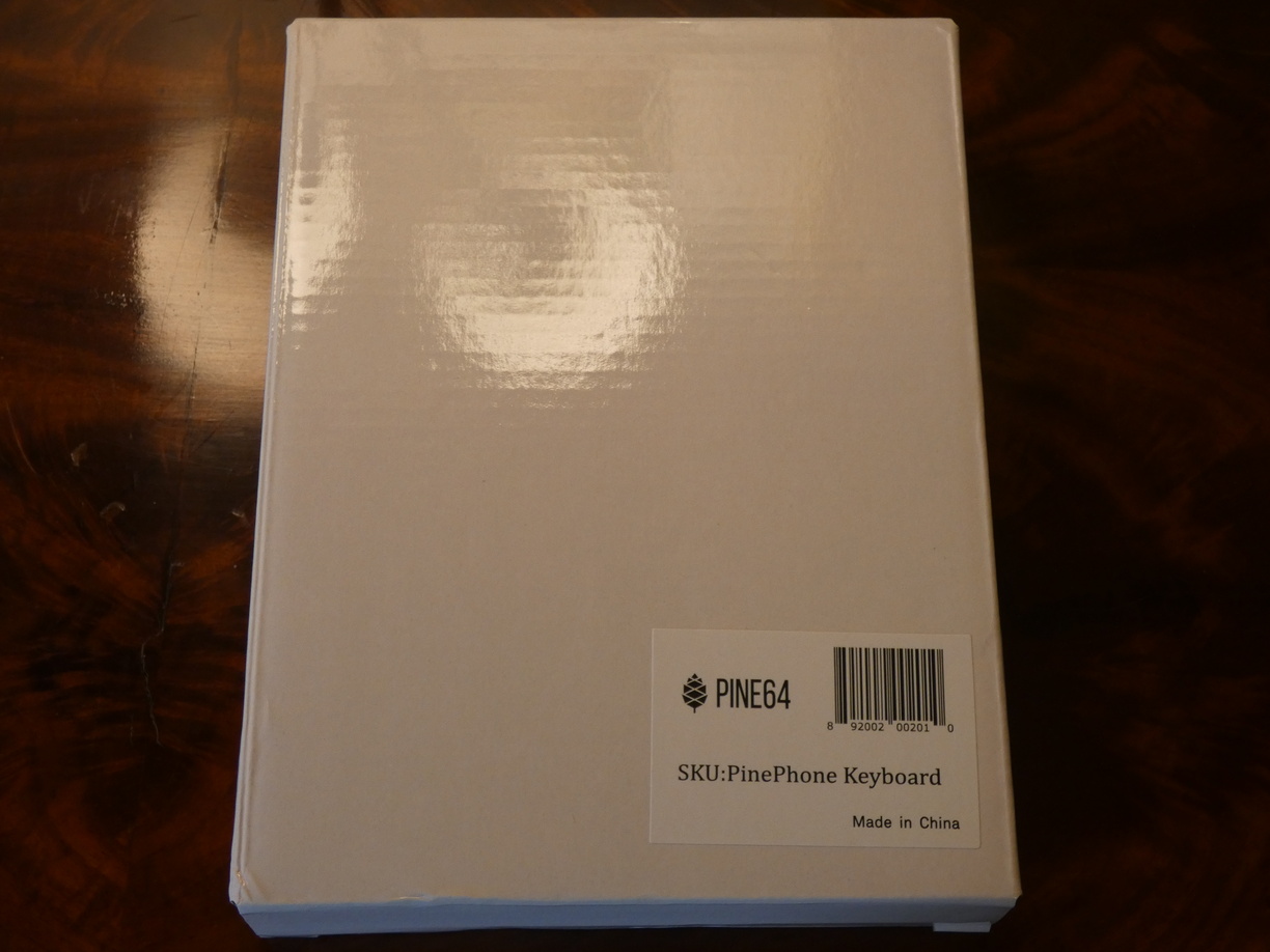 A photo of a flat white box with a barcode sticker saying 'Pine64, SKU: PinePhone Keyboard, Made in China'.